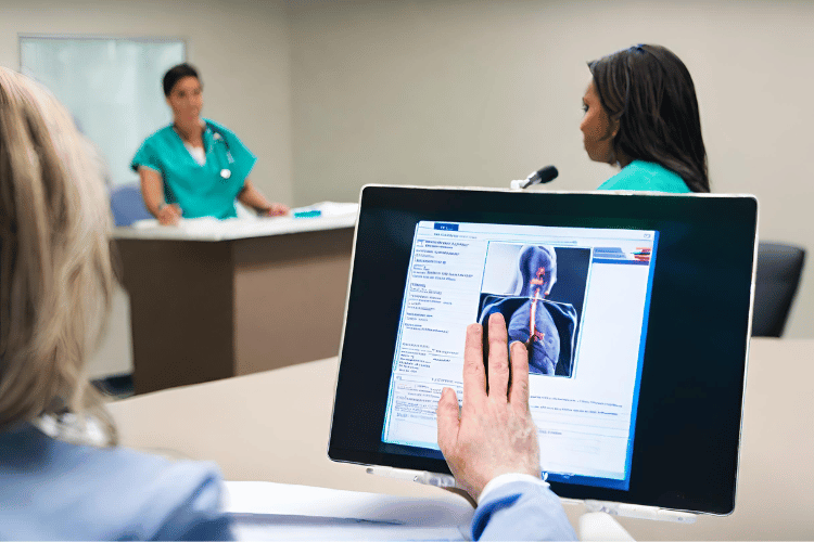 A person looks at an electronic medical records as two nurses speak in front of him.